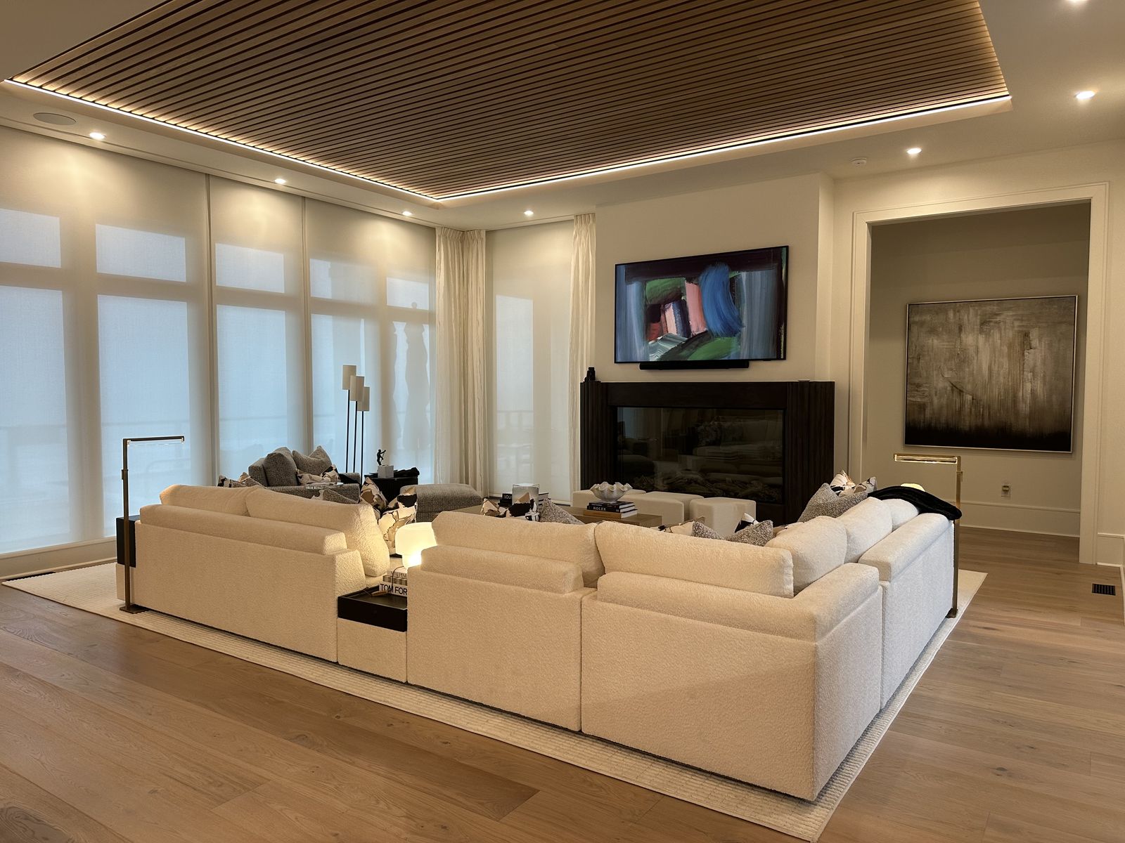 Living room TV installation above fireplace with LED accent lighting and motorized shades